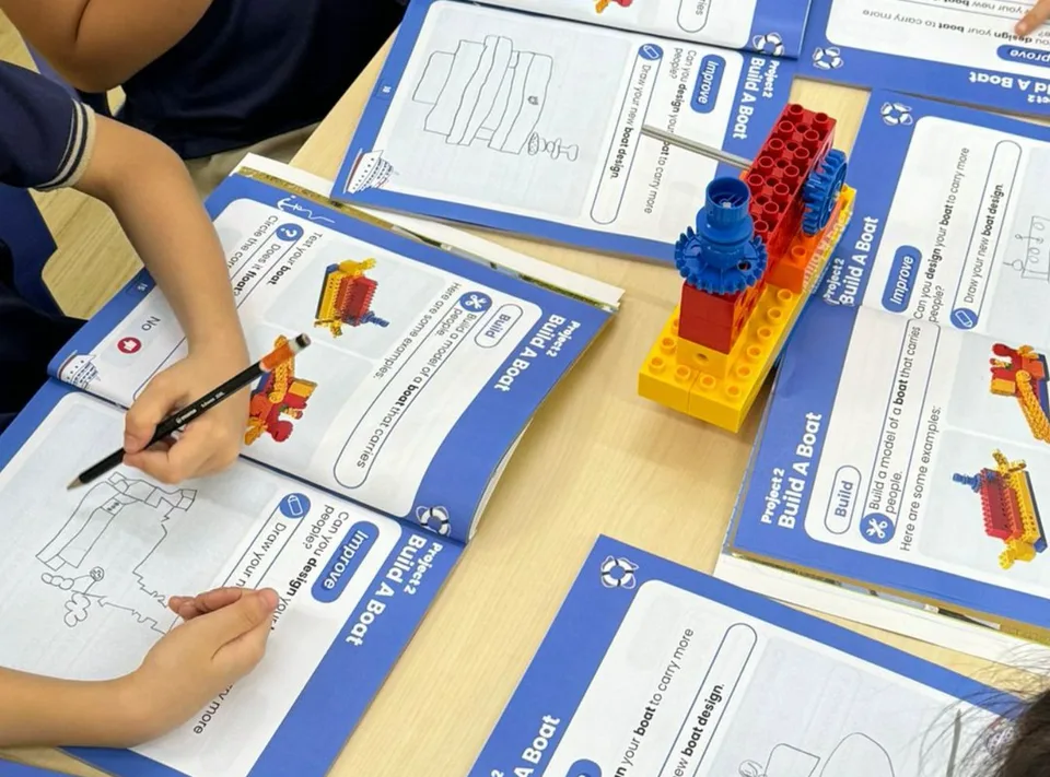 Workbooks open on a desk with a brick build and pencils, no faces